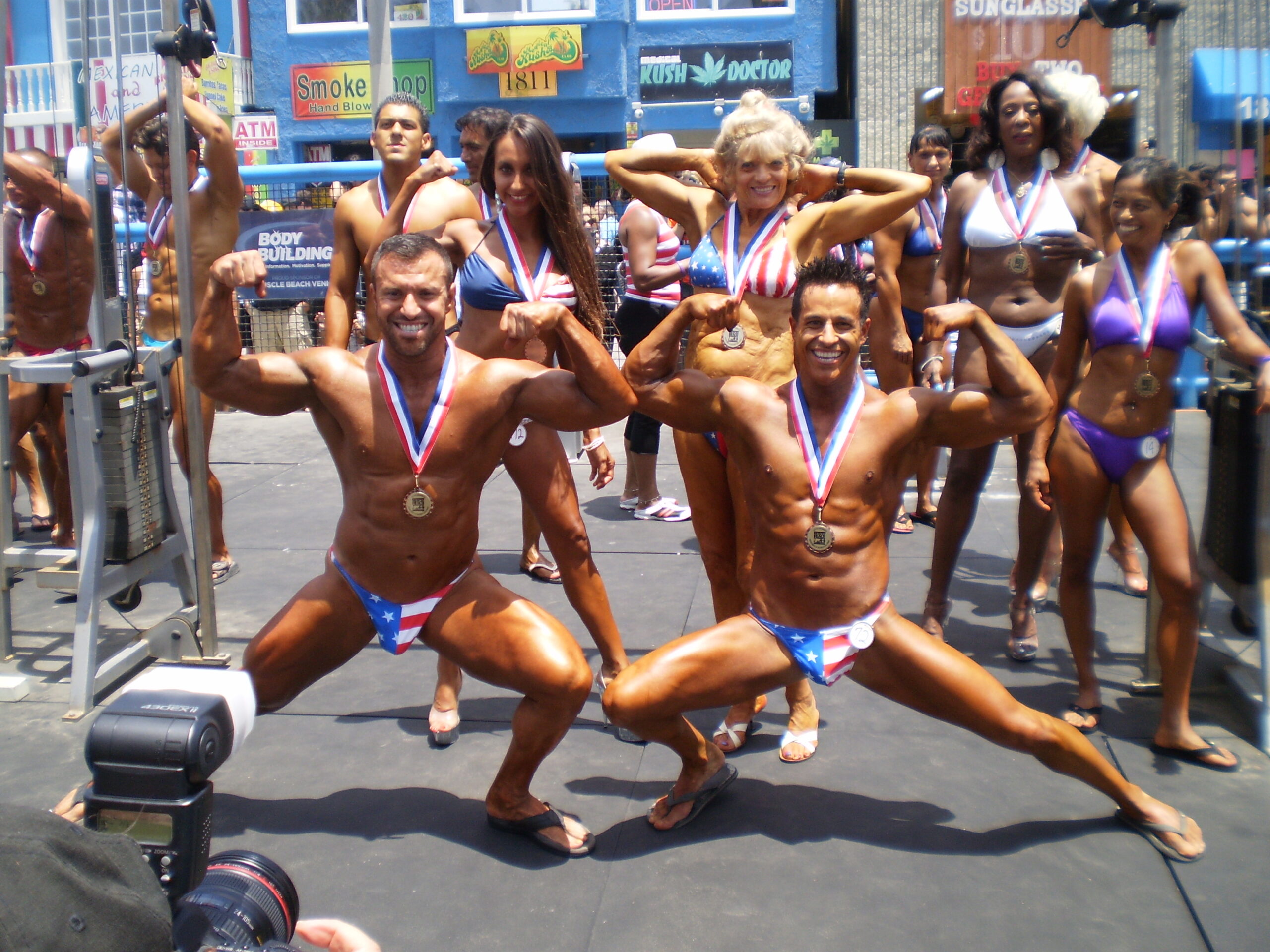BODYBUILDERS OF ALL AGES - MEN AND WOMEN POSING FOR PICTURE AT THE MUSCLE BEACH VENICE PEN ON THE 4TH OF JULY - MEN WEARING AKISTRO USA FLAG POSING TRUNKS